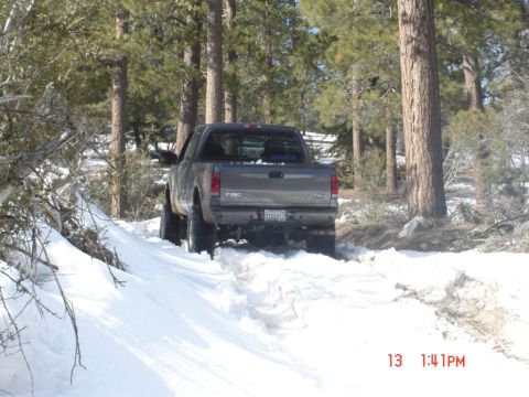 2000 Ford F-450 - A gray Ford F-250 Super Duty pickup truck navigates a snowy path through a forest.