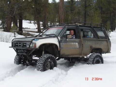 2000 Ford F-450 - A heavily modified SUV navigates a snowy terrain with its large tires digging into the snow.