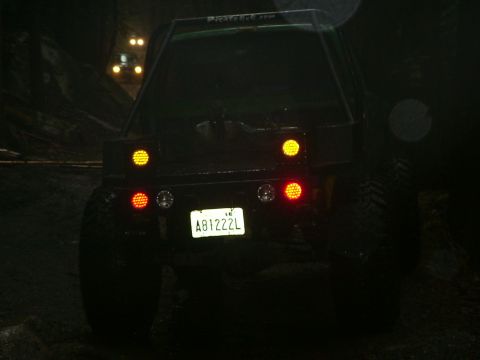 1990 Ford Bronco - This SUV's rear lights are illuminated while driving on a dark, wet road, with another vehicle in front.