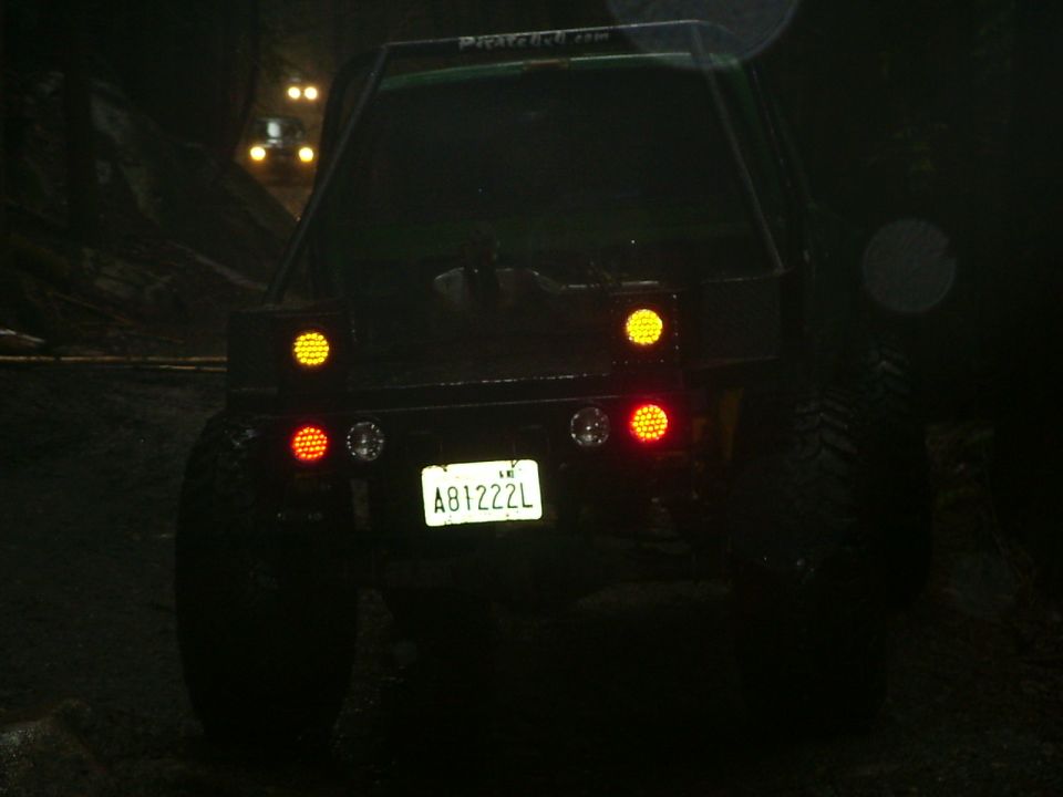Rear view of an off-road SUV with its brake lights on, driving in the dark. Another vehicle is visible ahead