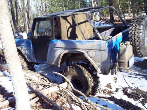 1974 Ford Bronco - A blue 1974 Ford Bronco is seen off-road, partially stuck in snow and mud with a roll cage and spare tire visible.