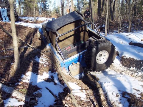 1974 Ford Bronco - An off-road vehicle navigates a challenging muddy and snowy trail in a wooded area.