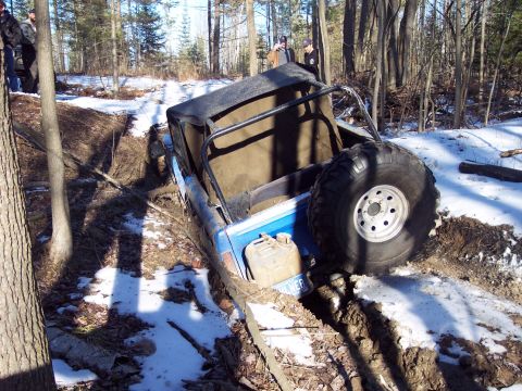 1974 Ford Bronco - An off-road vehicle is stuck in a muddy, wooded area with snow on the ground.