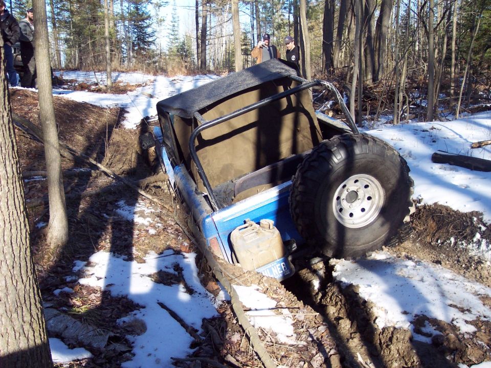 Blue off-road vehicle with a soft top stuck in a muddy ditch, spare tire visible
