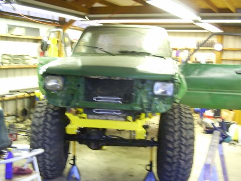 1990 Ford Bronco - This green SUV is undergoing repairs in a garage, with its front end removed and tires elevated.