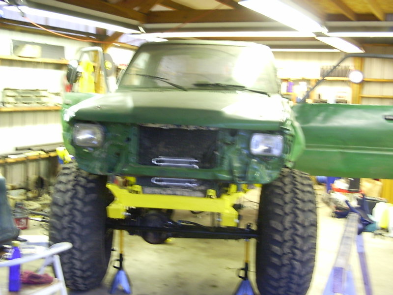 green SUV on jack stands, front end disassembled, large off-road tires