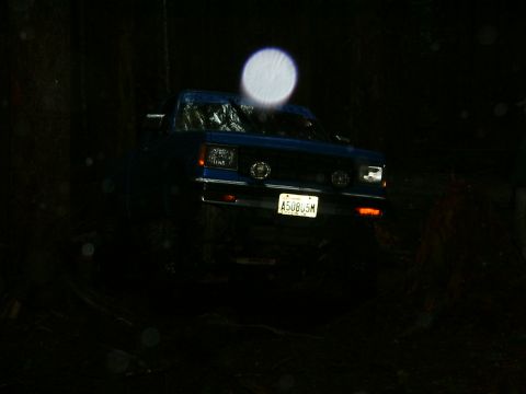 1990 Ford Bronco - A blue pickup truck is seen at night, its headlights illuminating the dark surroundings.