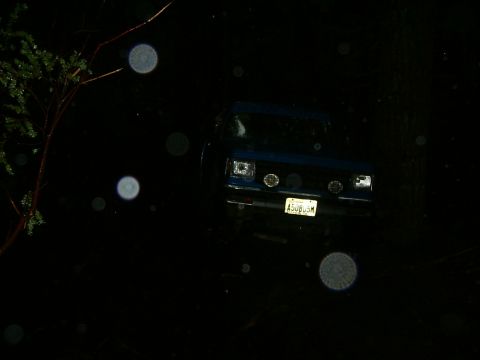 1990 Ford Bronco - A blue SUV is parked in the dark, illuminated by its headlights and some circular light artifacts.