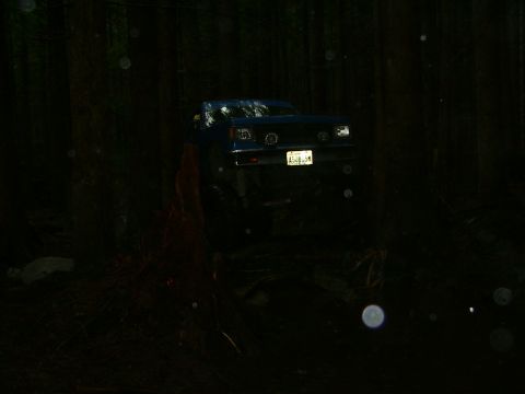 1990 Ford Bronco - A blue SUV navigates a dark, wooded trail at night, its license plate illuminated.