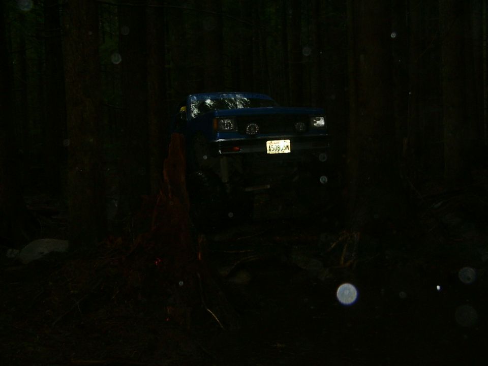 Blue SUV with a lifted suspension driving off-road at night. License plate is visible