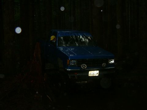 1990 Ford Bronco - Blue pickup truck driving off-road at night in a wooded area. The vehicle appears to be from the 1980s.
