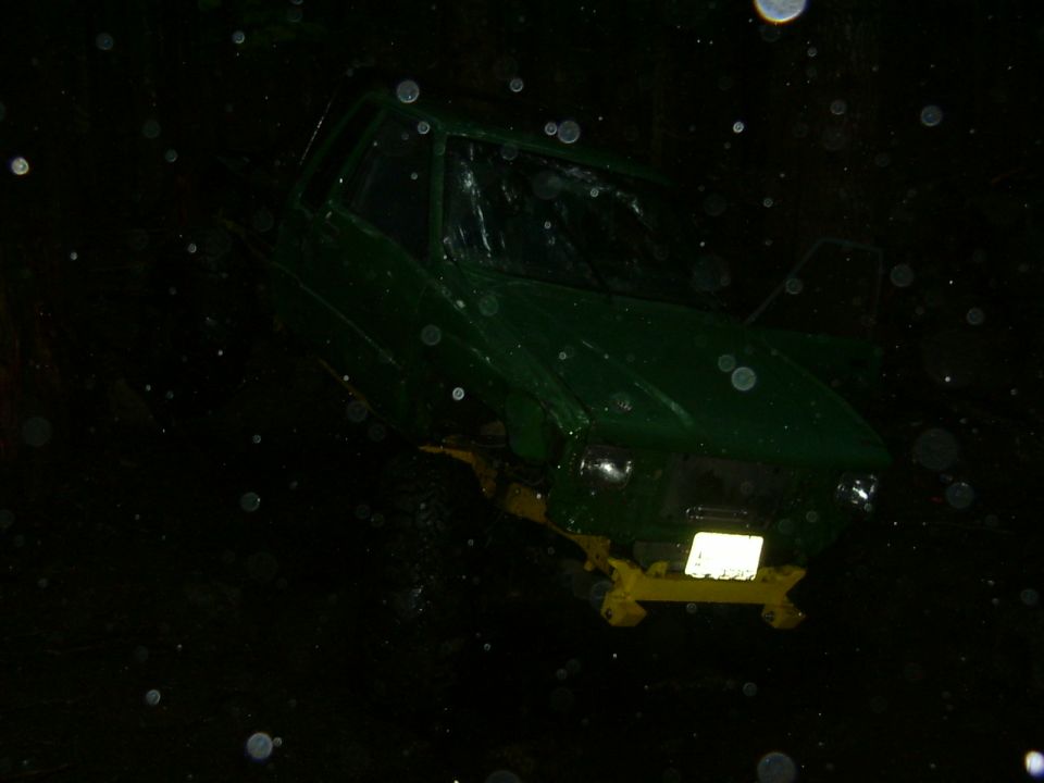 Green SUV with a damaged windshield and yellow tow hitch, viewed from the front at night