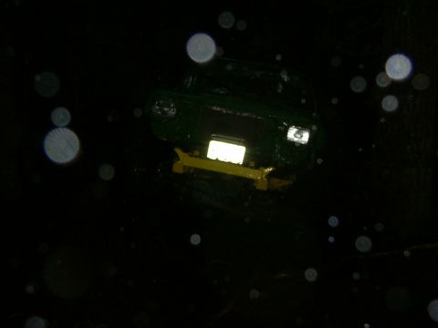 1990 Ford Bronco - A green vehicle is partially visible in the dark, a yellow bumper and illuminated front.