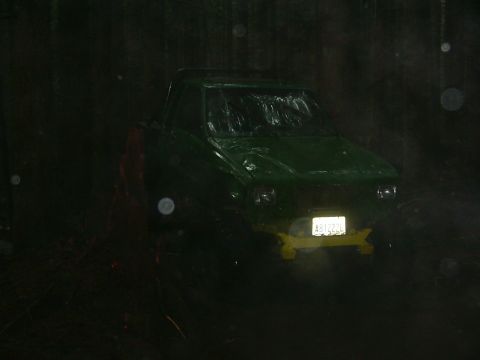 1990 Ford Bronco - A green pickup truck is visible at night, with rain falling and its headlights illuminated.