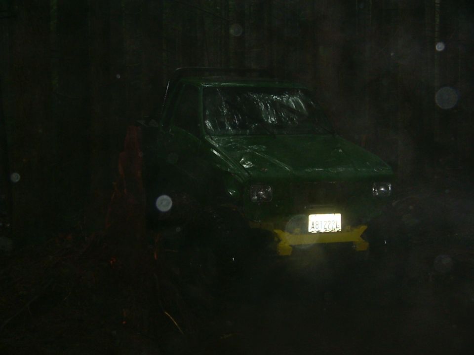 Green pickup truck with yellow bumper and license plate AB1222L, seen at night in the rain