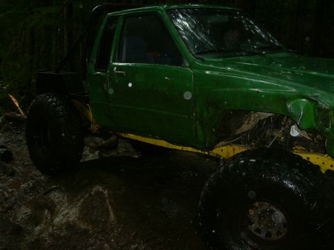 1990 Ford Bronco - This heavily modified truck sits in a wet, wooded environment, its large tires covered in mud.