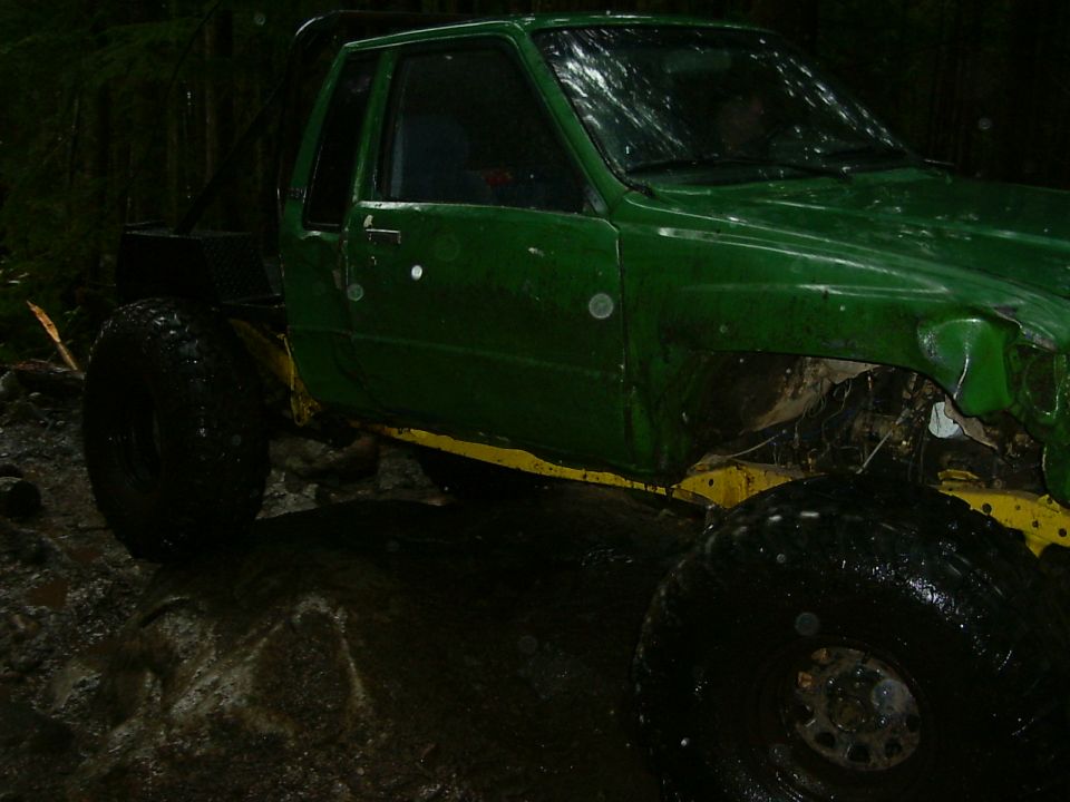 green off-road truck with large tires, in a muddy wooded area