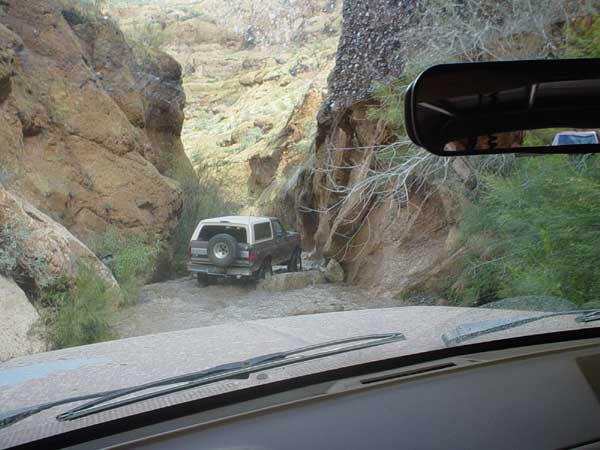 1989 Ford Bronco rear view driving through a rocky canyon stream