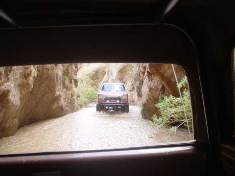 1989 Ford Bronco - Red Ford Bronco navigates a riverbed within a rocky canyon, likely a 1987 model.