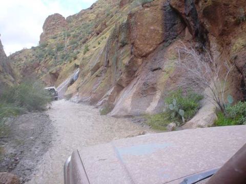 1989 Ford Bronco - Two vehicles navigate a wet, rocky canyon, with one vehicle in the foreground and another further ahead.