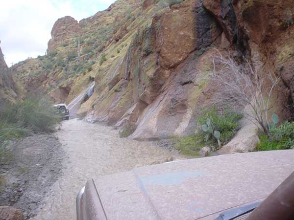 Two SUVs driving through a muddy canyon with a waterfall in the background