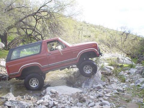 1989 Ford Bronco - A red Ford Bronco navigates a rocky stream bed in a dry, desert environment.