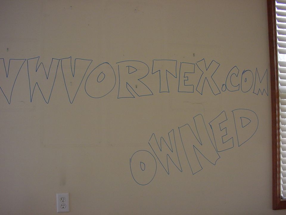 Wall with blue graffiti that reads "VWORTEX.COM OWNED" and a SuperMotors logo