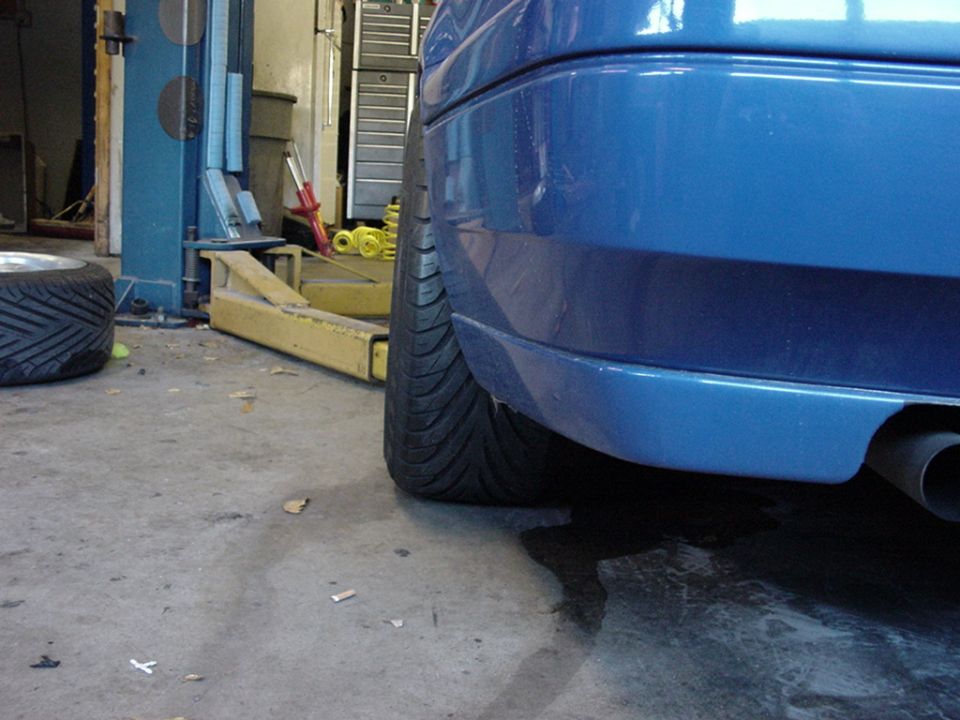 Close-up of a blue car's rear bumper and tire, with a tire and rim visible on the left