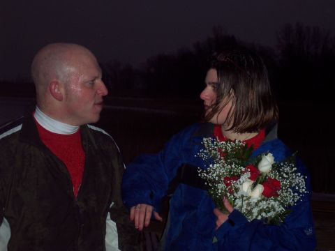 1987 Ford Bronco - A man and woman stand close together outdoors at night, with the woman holding a bouquet of flowers.