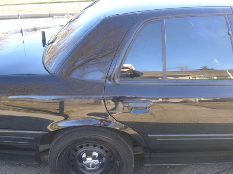1999 Ford Crown Victoria - Side view of a black sedan with steel wheels and tinted windows.