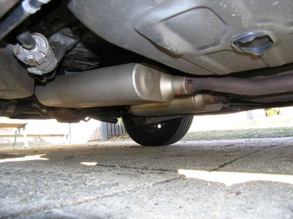 Underside view of vehicle exhaust system with silver muffler and rusty piping