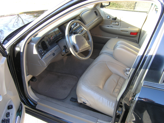 Interior of a 1999 Ford Crown Victoria, showing tan leather seats, dashboard, and steering wheel