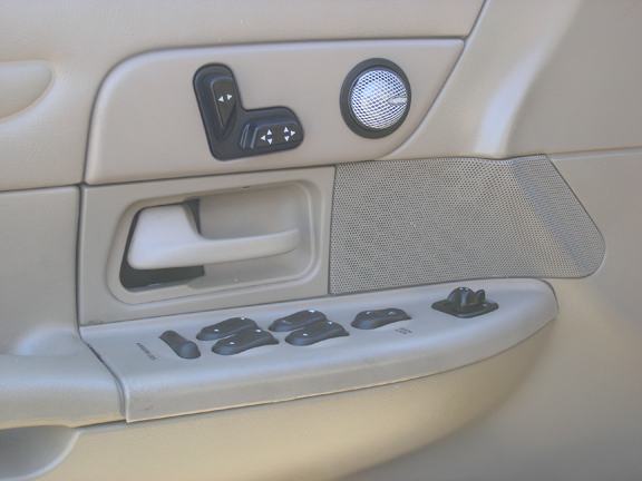 Tan driver's door panel with power window switches, seat controls, tweeter and door handle