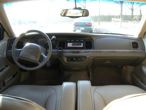 1999 Ford Crown Victoria - The interior of a car shows tan seats and a dashboard with an aftermarket radio, while another car is visible through the windshield.