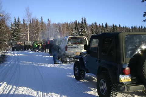 2003 Jeep TJ - A line of off-road vehicles, including a blue Jeep TJ, are parked on a snowy trail under a clear blue sky.