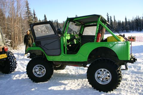 2003 Jeep TJ - A bright green, heavily modified Jeep sits in a snowy landscape next to another vehicle.