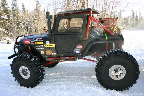 2003 Jeep TJ - Modified Jeep Wrangler with custom roll cage and off-road tires sits in a snowy landscape.