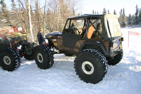 2003 Jeep TJ - A modified Jeep Wrangler with massive tires sits in the snow next to another off-road vehicle.