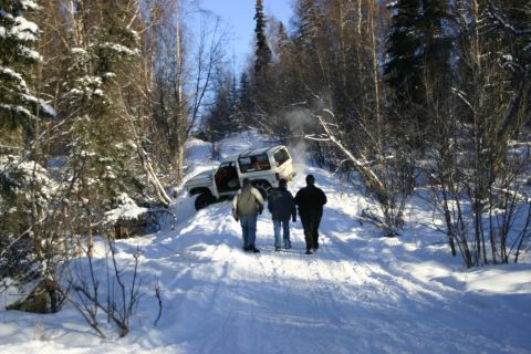 2003 Jeep TJ - A white SUV is stuck in the snow on a hill, with three people approaching it.