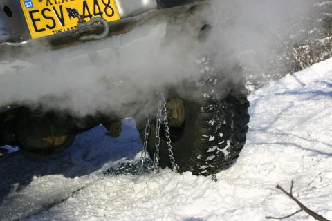 2003 Jeep TJ - A vehicle's rear tire is shown with snow chains and emitting smoke in a snowy environment.