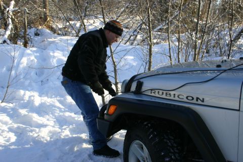 2003 Jeep TJ - Man connects a cable to the hood of a 2003 Jeep TJ Rubicon in a snowy wooded area.