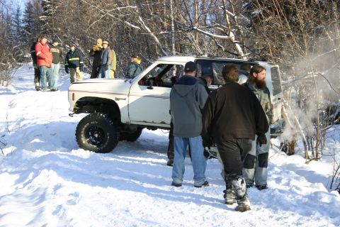 2003 Jeep TJ - A group of people stand around a white off-road vehicle partially submerged in snow during a winter outing.
