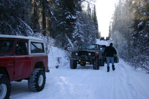2003 Jeep TJ - Several off-road vehicles drive down a snow-covered path through a forest.