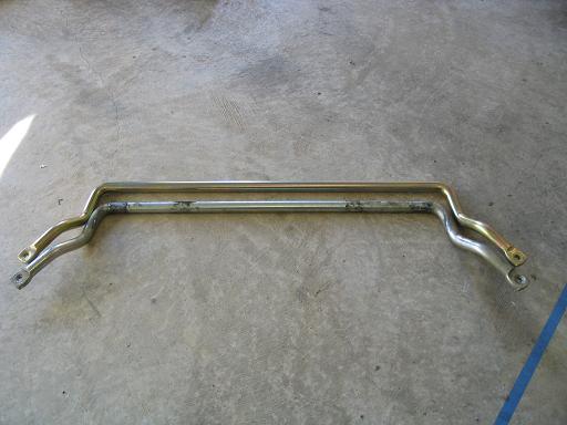 Two metal bars, one above the other, on a concrete floor. The top bar is gold-colored, the bottom is silver and shows wear