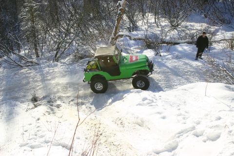 2003 Jeep TJ - A green Jeep navigates a snowy trail with a person standing in the background.
