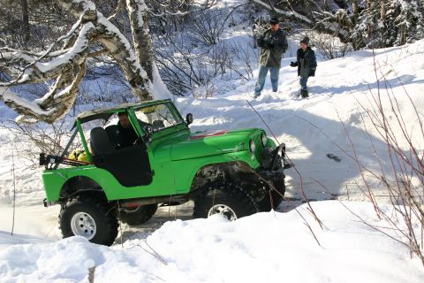 2003 Jeep TJ - A bright green Jeep CJ-5 navigates a snowy trail, with two onlookers observing from the bank.