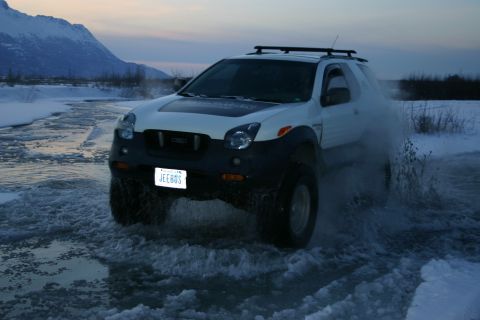 2003 Jeep TJ - A white SUV navigates through icy water with a mountain in the background.