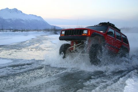 2003 Jeep TJ - A red Jeep Cherokee navigates through a partially frozen body of water, kicking up spray.
