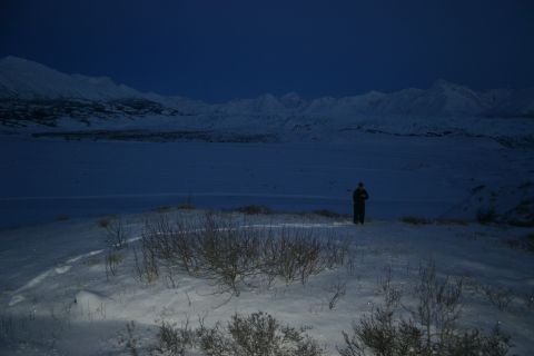 2003 Jeep TJ - A lone figure stands in a vast, snow-covered landscape under a deep blue twilight sky, with mountains in the distance.