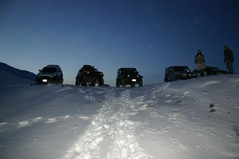 2003 Jeep TJ - A group of off-road vehicles are parked on a snow-covered hill at dusk.